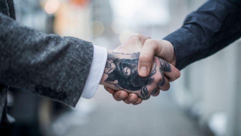 An employee with visible tattoos sitting around a table talking with colleagues