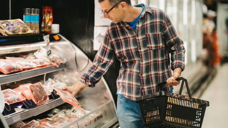 Middle age adult man with a shopping basket in a supermarket buying meat