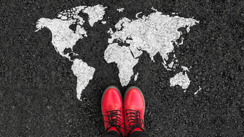 World map on an asphalt road. Top view with view of person’s red shoes.