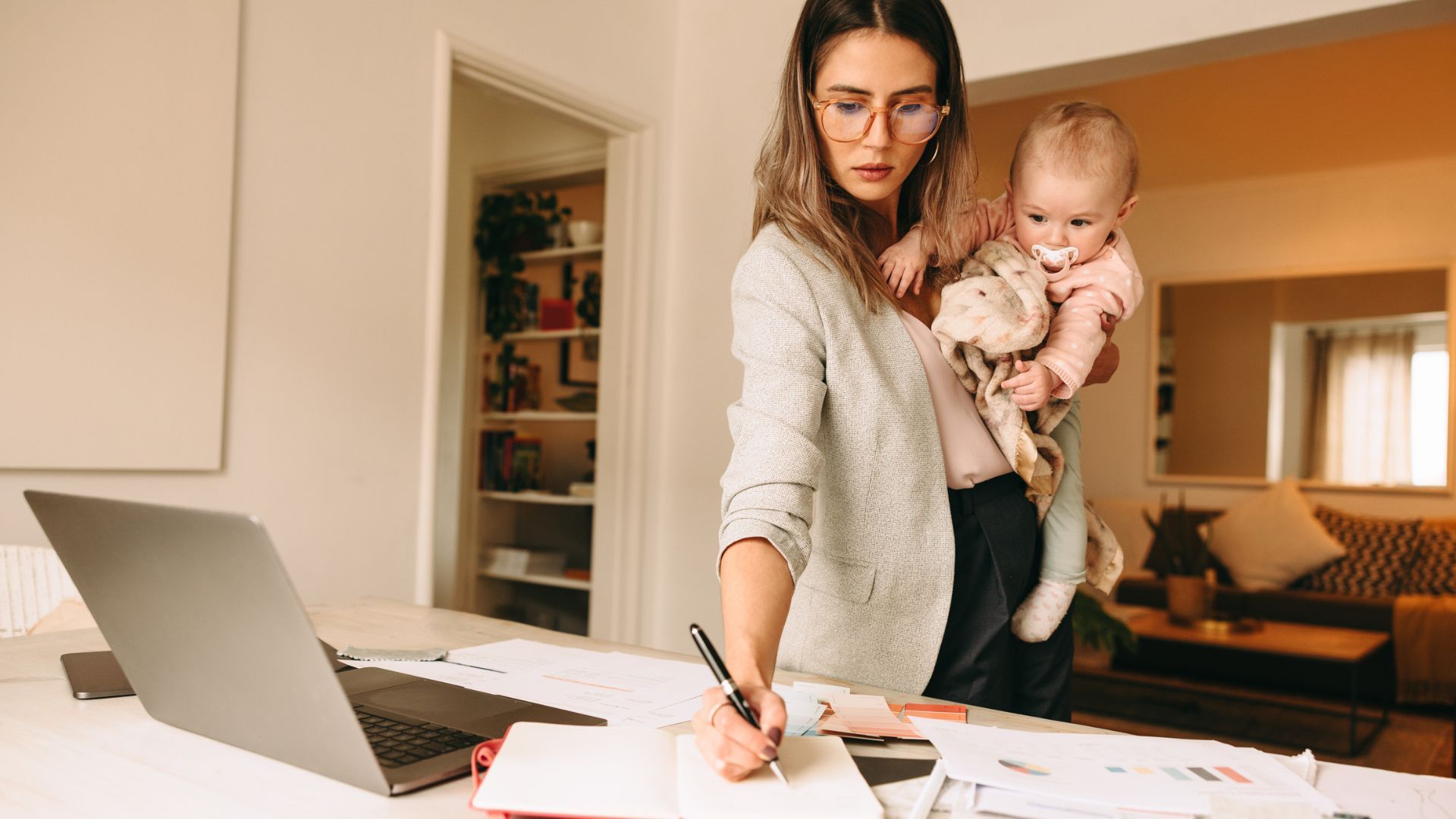 Female professional making notes while holding her baby, balancing work and motherhood