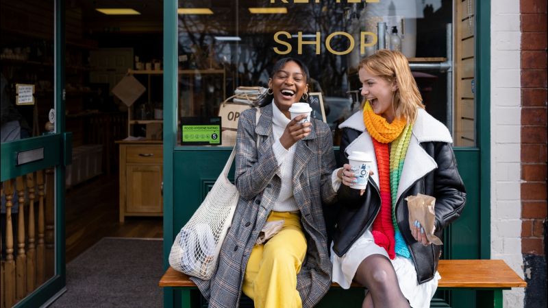 Two friends sitting outside a café laughing and drinking coffee. 