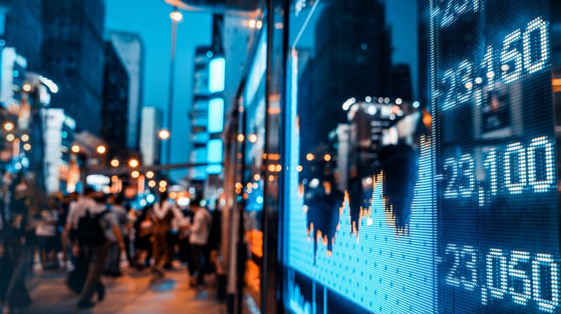 Display of stock market quotes with city scene reflected on glass.