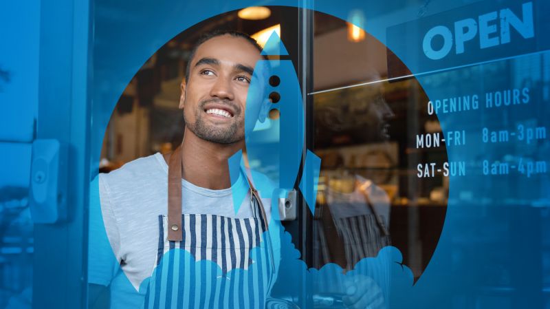 Smiling man looks out through the front window of his business