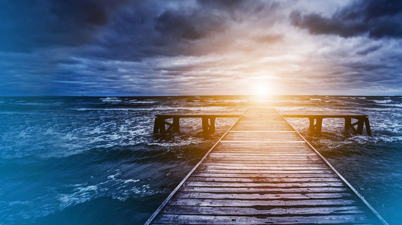 Old wooden jetty during storm on the ocean. Abstract light at the end. 