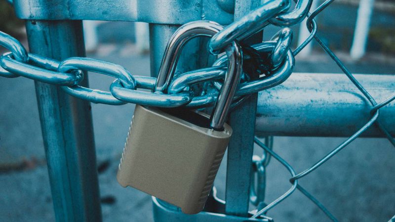 Locked gate tethered by metal chain and padlock.