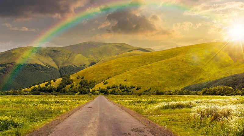  landscape with an abandoned asphalt road that rolls through meadows with sunset light and rainbow.