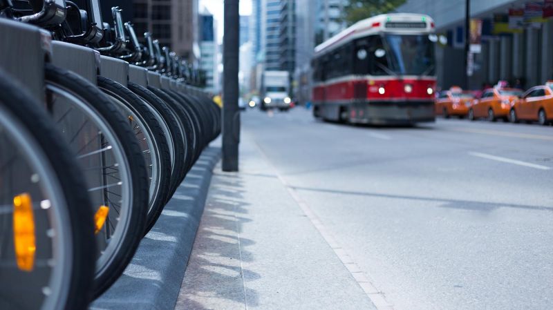 Toronto streetcar in the distance coming down a street with parked taxis and a row of bike wheels at a rental station.