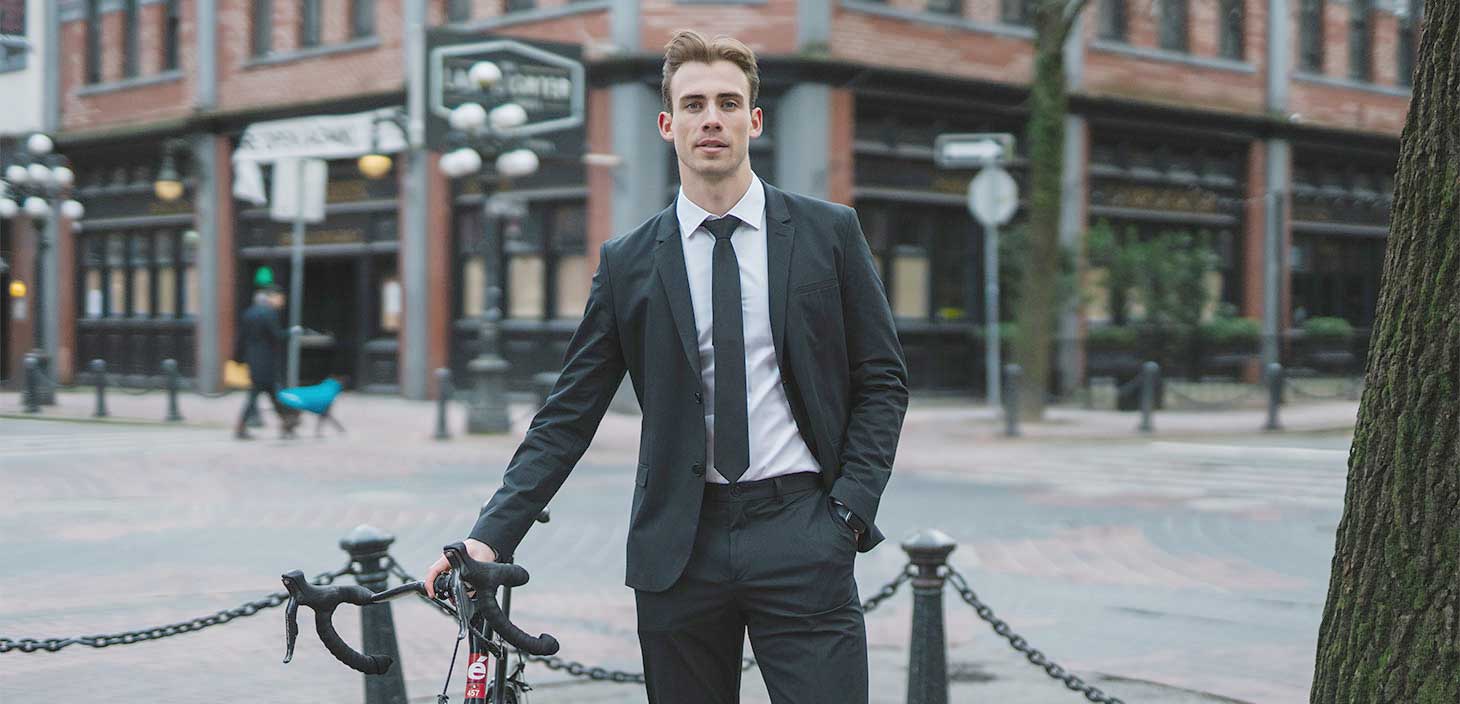 Connor Emery is a man in a nice suit with styled brown hair. He is suspended in the air in a running pose in front of a brick wall.