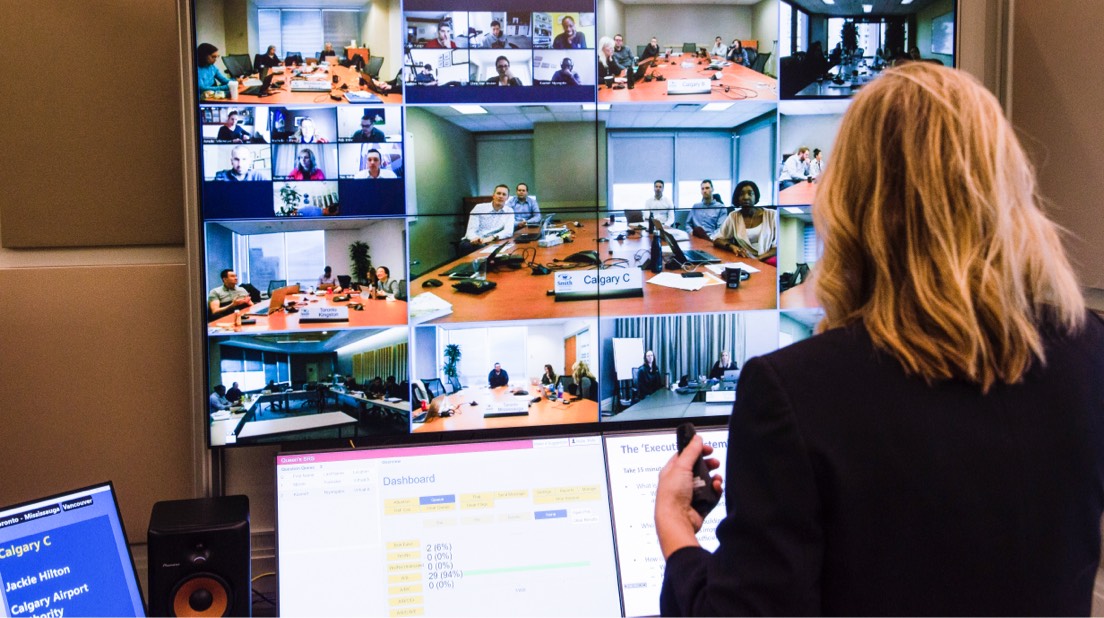 A professor in front of a screen, teaching groups of remote teams